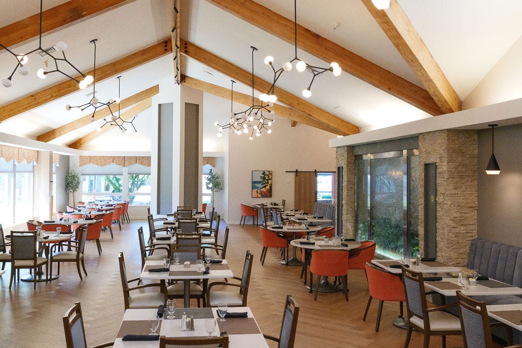 Main dining room at McLoughlin Place with a vaulted ceiling, exposed beams, a stone column and orange and grey chairs