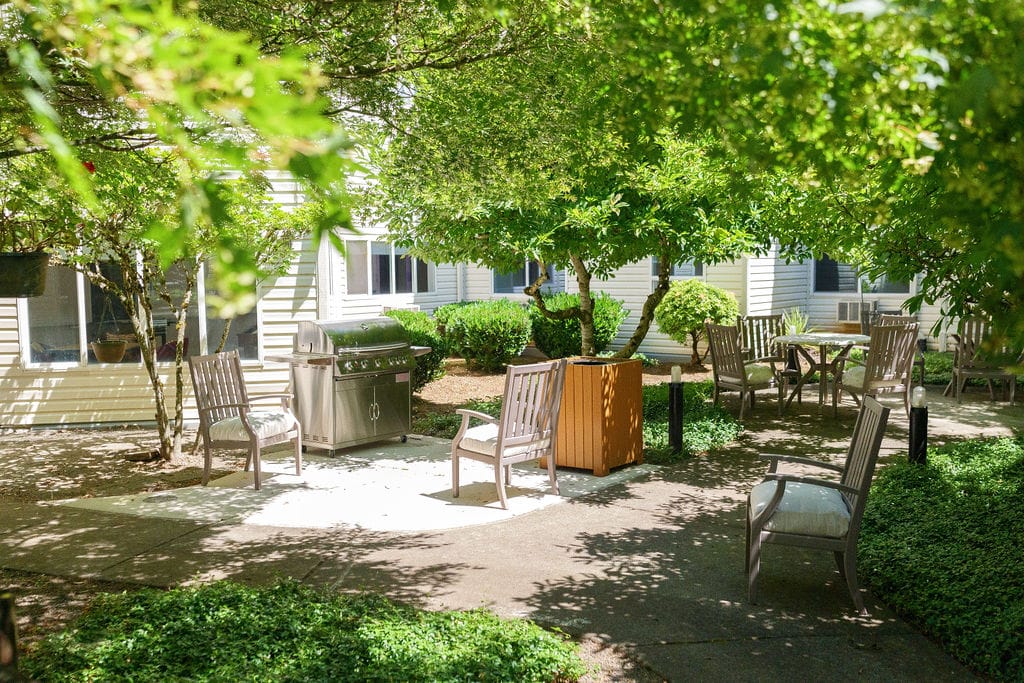Outdoor courtyard with a gas grill and patio seating under mature trees