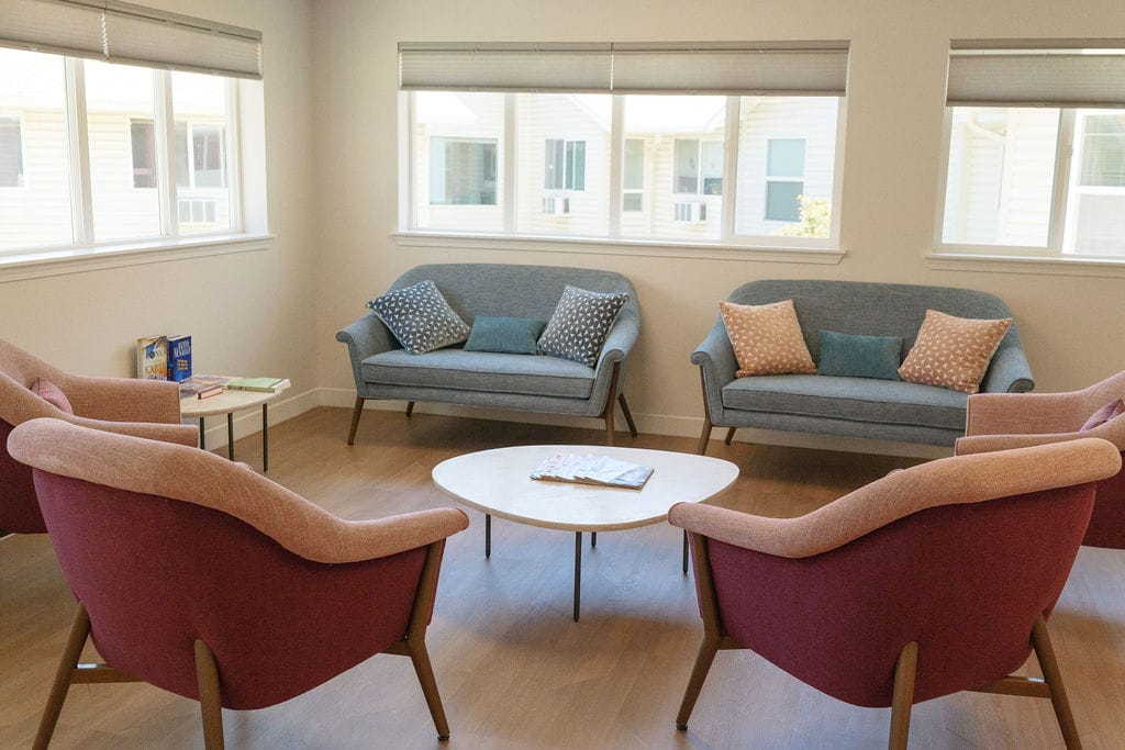 Sitting room at McLoughlin Place with two grey sofas and pink armchairs around a low oval table beneath a bank of windows
